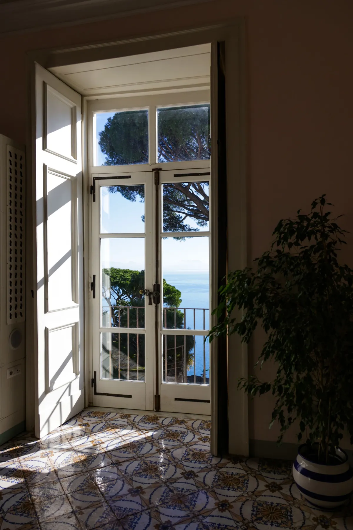 Una porta aperta verso un balcone, tra luce naturale e pavimenti decorati