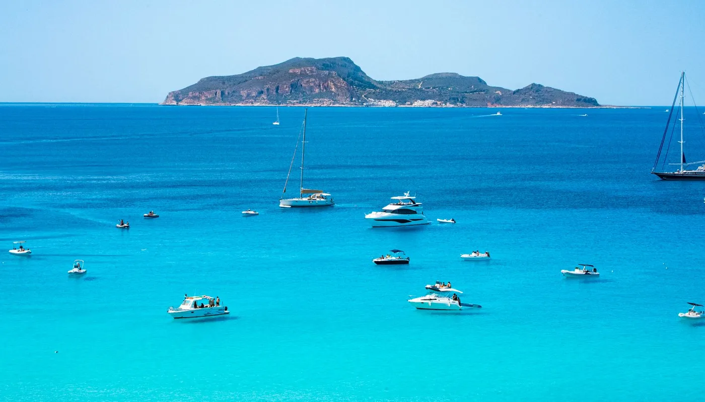 Il mare siciliano turchese con barche e un’isola all’orizzonte
