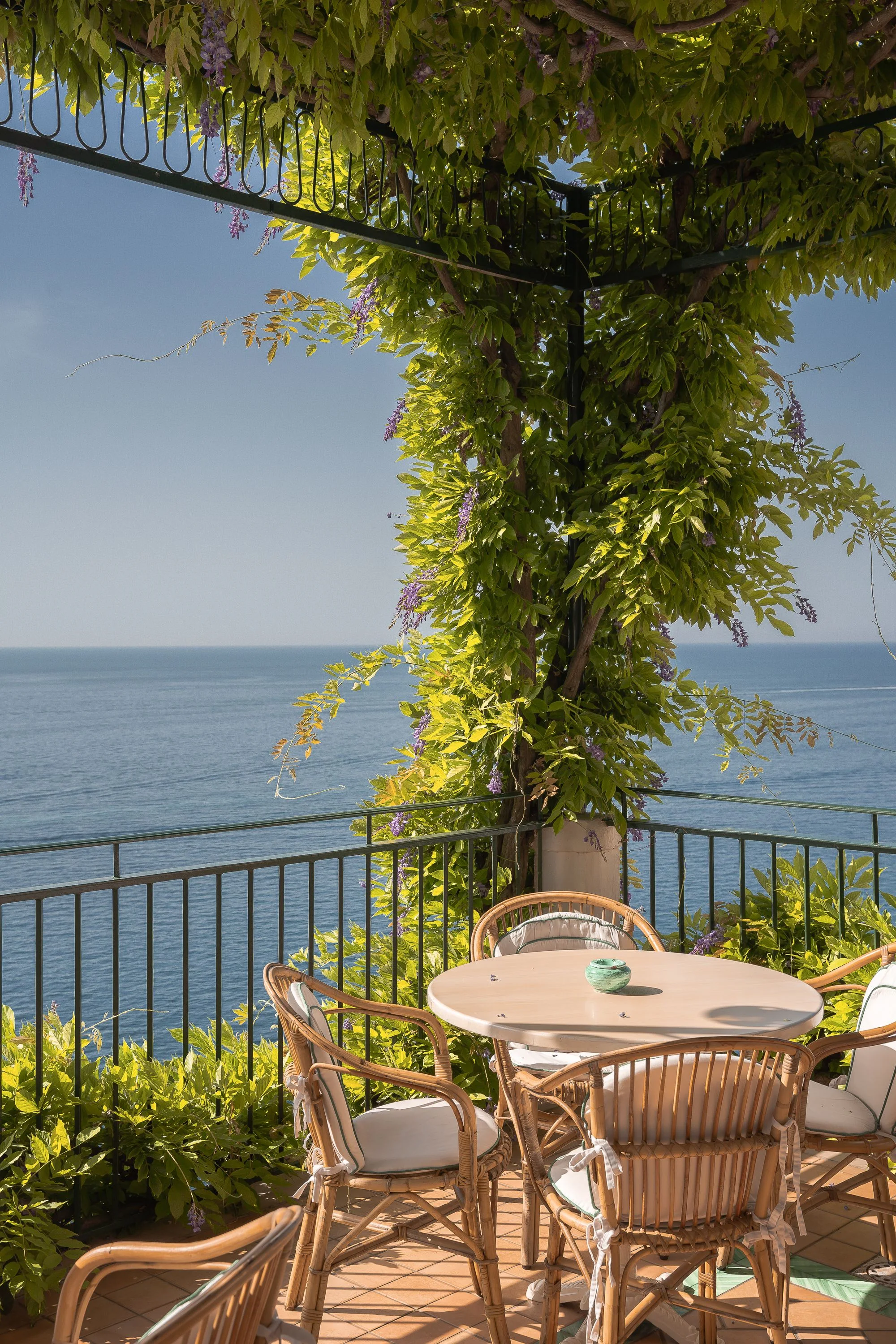 Una terrazza mediterranea con sedie in vimini, piante e vista sul mare
